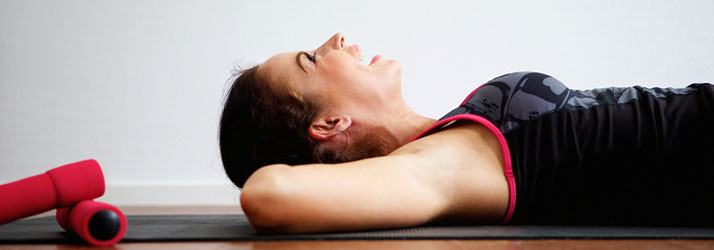 Person resting on an exercise mat beside a foam roller.